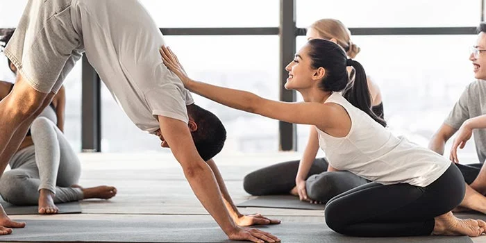 female-coach-correcting-hatha-yoga-beginner-at-group-class